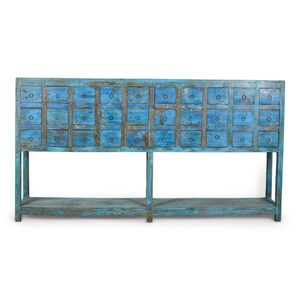 May include: A blue, distressed wooden cabinet with multiple small drawers. The cabinet is rectangular, featuring a lower shelf, and is painted in a weathered, rustic style. Each drawer has a small, round pull.