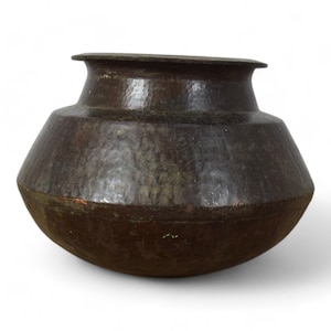 May include: A dark brown, hammered metal pot with a wide, rounded body and a narrow, flared rim. The surface features a textured, dimpled finish across the exterior, showing signs of age and oxidation with subtle variations in colour tone.