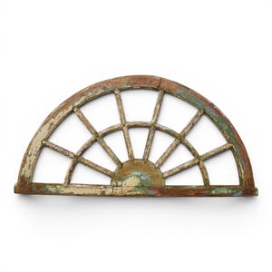 May include: A semi-circular wooden window frame featuring a sunburst design with multiple spokes. The wood displays a weathered, distressed finish with visible layers of chipped paint in shades of brown, green, and off-white throughout the structure.
