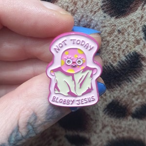 May include: Pink enamel pin with a cartoon character wearing a blanket and the text "Not Today, Blobby Jesus".