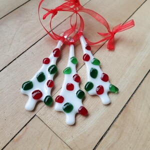 Peut inclure: Trois décorations de Noël en verre blanc avec des pois rouges et verts. Les décorations sont suspendues à un ruban rouge.