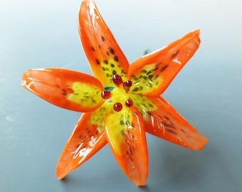 May include: A glass lily flower with orange and yellow petals and black spots. The flower has a red center with small, round, red dots.