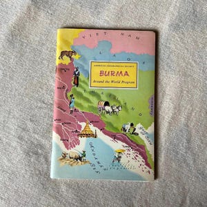 Op de afbeelding: Vintage reisgids getiteld "BURMA Around the World Program" van de American Geographical Society. De omslag toont een kleurrijke kaart van Birma met illustraties van lokale scènes en bezienswaardigheden. De gids is in goede staat.