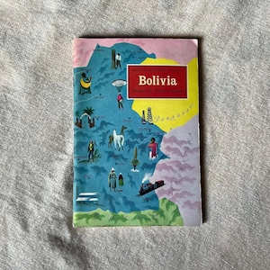 以下が含まれることがあります： 「Bolivia Around the World Program」と題されたヴィンテージ旅行ガイド。表紙には、人々、動物、ランドマークのイラストが描かれたボリビアの地図が描かれています。カラーパレットには、青、黄、赤、ピンクが含まれています。