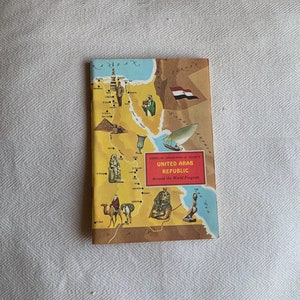 Op de afbeelding: Een vintage kaart van de Verenigde Arabische Republiek, uitgegeven door de American Geographical Society als onderdeel van hun Around the World Program. De kaart toont een gestileerde illustratie van het land met bezienswaardigheden, waaronder de Sfinx en de piramides.