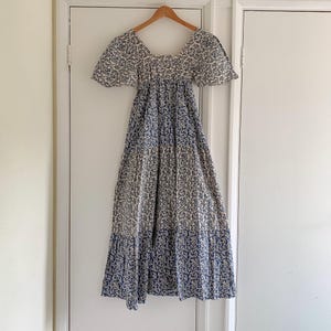 May include: A white and blue floral print maxi dress with a square neckline and short puff sleeves. The dress has a tiered skirt and a fitted bodice.