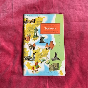 Op de afbeelding: Een kleurrijke geïllustreerde kaart van Denemarken met de tekst "American Geographical Society Around the World Program" en de titel "Denmark". De kaart toont verschillende bezienswaardigheden en symbolen, waaronder een windmolen, een zeemeermin, een kasteel en een Vikingschip.