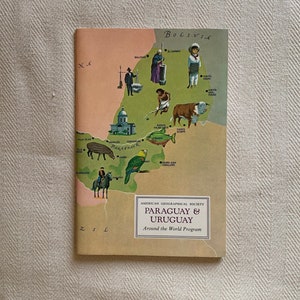 Op de afbeelding: Een vintage reisgids getiteld "Paraguay & Uruguay" van de American Geographical Society. De omslag toont een kaart met illustraties van mensen, dieren en bezienswaardigheden. De gids staat tegen een neutrale achtergrond.