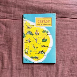 Op de afbeelding: Een vintage kaart van Ceylon, nu Sri Lanka, uit het programma "Around the World" van de American Geographical Society. De kaart toont een gele omtrek van het eiland met verschillende steden en dorpen die in zwarte tekst zijn gelabeld.