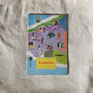 May include: A colourful illustrated map of Argentina, part of the American Geographical Society's Around the World Programme. The map features various landmarks and animals, including a ship, a cow, a cactus, and an alligator.