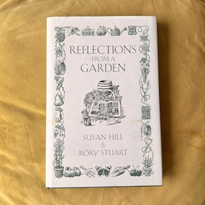 以下が含まれることがあります： スーザン・ヒルとローリー・スチュアートによる「Reflections From a Garden」というタイトルのハードカバー本。表紙には、庭の道具、植物、額縁に入ったシーンの詳細な白黒イラストが描かれています。本は黄色の背景に置かれています。