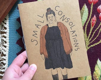 Könnte beinhalten: Ein braunes Papierheft mit dem Text "SMALL CONSOLATIONS" auf dem Umschlag. Der Umschlag zeigt eine handgezeichnete Illustration einer Person, die einen braunen Cardigan und ein schwarzes Kleid trägt.