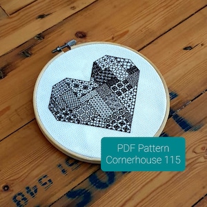 Puede incluir: Un patrón de punto de cruz en blanco y negro de un corazón geométrico en un aro de bordado de madera. El patrón se titula "Cornerhouse 115" y está disponible para descargar en PDF.