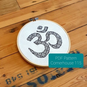 May include: A black and white cross-stitch embroidery of the Om symbol in a round wooden embroidery hoop. The hoop is on a wooden surface. The text "PDF Pattern Cornerhouse 115" is visible in the lower right corner of the image.