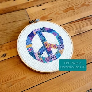 May include: A white embroidery hoop with a colorful peace sign design. The peace sign is made up of different colored squares and is surrounded by a white background. The text "PDF Pattern Cornerhouse 115" is visible in the bottom right corner of the image.