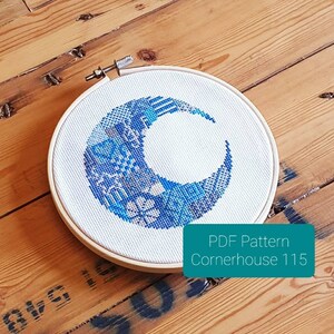 Może przedstawiać: Białe tamborek do haftu z wzorem półksiężyca w kolorze niebieskim i białym. Tamborek leży na drewnianej powierzchni. Pod tamborkiem znajduje się tekst "PDF Pattern Cornerhouse 115".