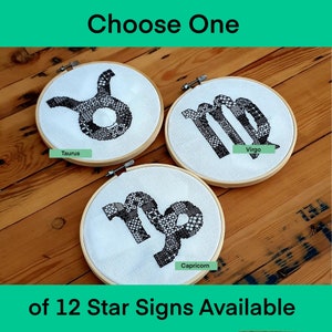May include: Three embroidery hoops featuring black and white zodiac signs. The signs are Taurus, Virgo, and Capricorn. The hoops are displayed on a wooden surface. Choose One of 12 Star Signs Available.
