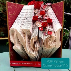 May include: A handcrafted book art piece with pages folded to spell "LOVE". Adorned with red paper roses and decorative accents. The background features a burgundy cover with the word "Christmas" and the text "Night". The base includes the text "I'm dreaming of a white Christmas".
