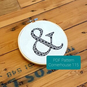 May include: A round embroidery hoop with a cream-colored fabric featuring a black ampersand design. The ampersand is filled with small floral patterns. The text "PDF Pattern Cornerhouse 115" is on a teal rectangle.