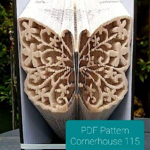 Op de afbeelding: Een boek met gevouwen pagina's die een vlinderontwerp vormen. De vlinder staat centraal in het open boek, met ingewikkelde patronen. Een turquoise label leest "PDF Pattern Cornerhouse 115".