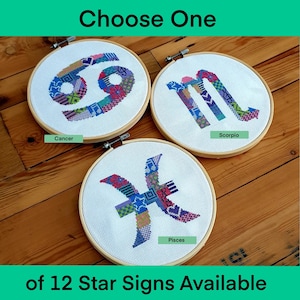 May include: Three embroidery hoops with colourful cross-stitch designs of the zodiac signs Cancer, Scorpio, and Pisces. The hoops are on a wooden surface. Choose One of 12 Star Signs Available.