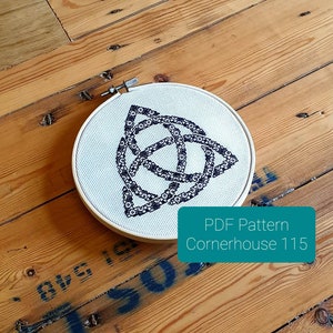 May include: A white embroidery hoop with a black and white Celtic knot design. The hoop is on a wooden surface. The text "PDF Pattern Cornerhouse 115" is below the hoop.