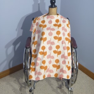 May include: A white wheelchair with a brown and orange patterned blanket draped over the back. The blanket has a floral design with pink and orange flowers.