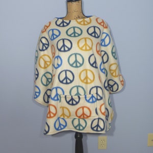 May include: A white fleece poncho with a peace sign pattern in blue, green, orange, and yellow. The poncho has a pocket on the front.