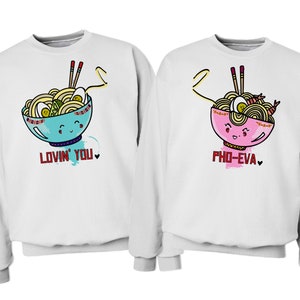 May include: Two white sweatshirts with a cartoon noodle bowl design. One sweatshirt says "Lovin' You" and the other says "Pho-Eva".