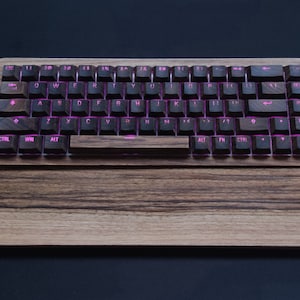 Op de afbeelding: Een houten toetsenbord met een donkerbruine afwerking en roze verlichte toetsen. Het toetsenbord heeft een bijpassende houten polsensteun.