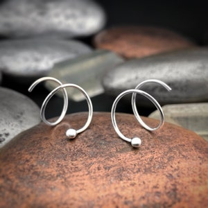 May include: A pair of silver hoop earrings with a twisted design and a small ball at the end of each hoop.