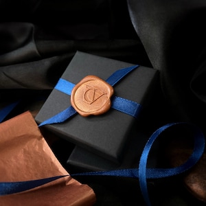 May include: A black gift box with a blue ribbon and a brown wax seal with the initials "CV" on it.
