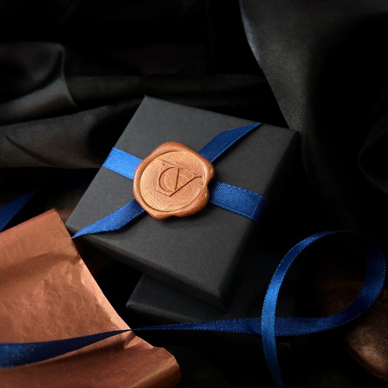 May include: A black gift box with a blue ribbon and a brown wax seal with the initials "CV" on it.