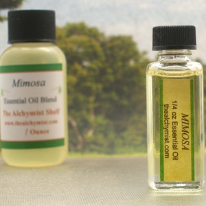 May include: Two small glass bottles with amber liquid and black caps. The bottles are labeled "Mimosa Essential Oil Blend" and "Mimosa 1/4 oz Essential Oil thealchymist.com".