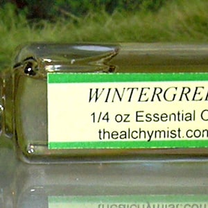 May include: A clear glass bottle with a black cap containing Wintergreen essential oil. The label reads "Wintergreen 1/4 oz Essential Oil thealchymist.com"