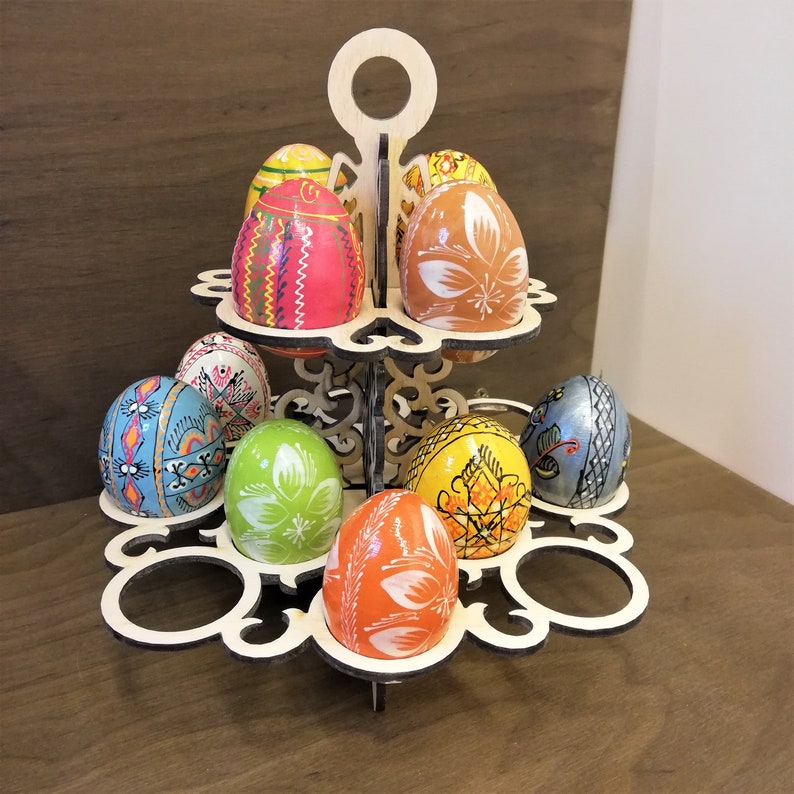 May include: A two-tiered wooden egg holder with a decorative design. The holder is filled with colorful, hand-painted Easter eggs.
