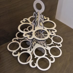 May include: A wooden tiered cupcake stand with a handle. The stand has a decorative design and is made of light brown wood.