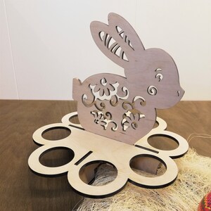May include: Wooden Easter egg holder shaped like a bunny with floral details. The holder has six egg-shaped compartments.