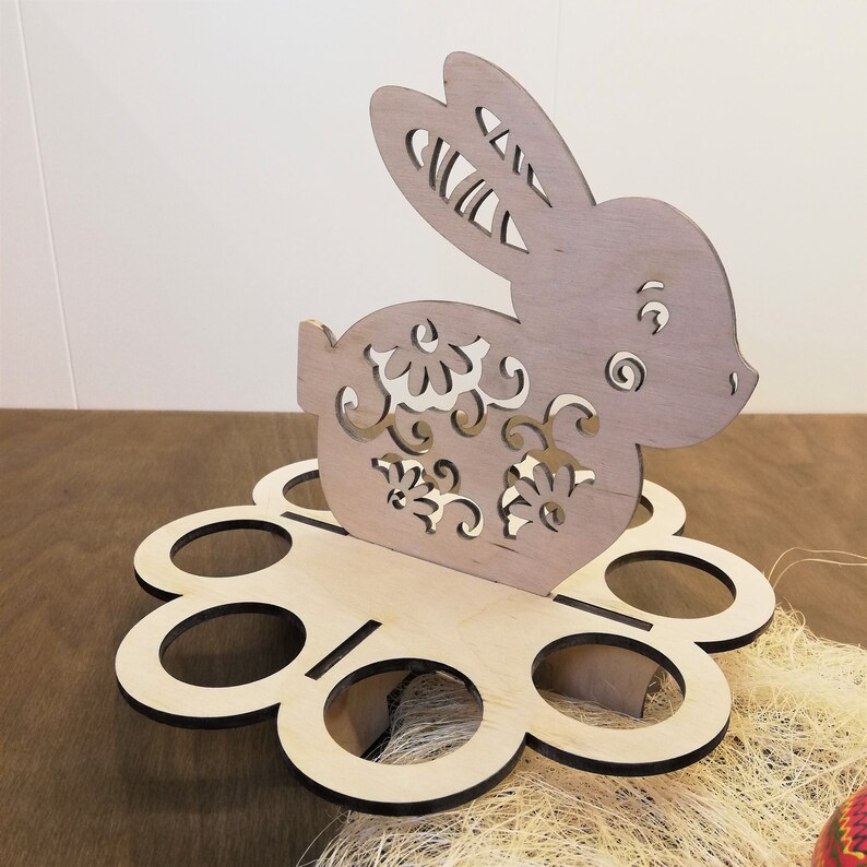 May include: Wooden Easter egg holder shaped like a bunny with floral details. The holder has six egg-shaped compartments.