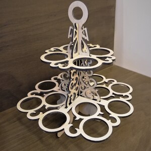 May include: A two-tiered wooden stand with a decorative design. The stand has a handle on top and 12 circular cutouts for holding items.