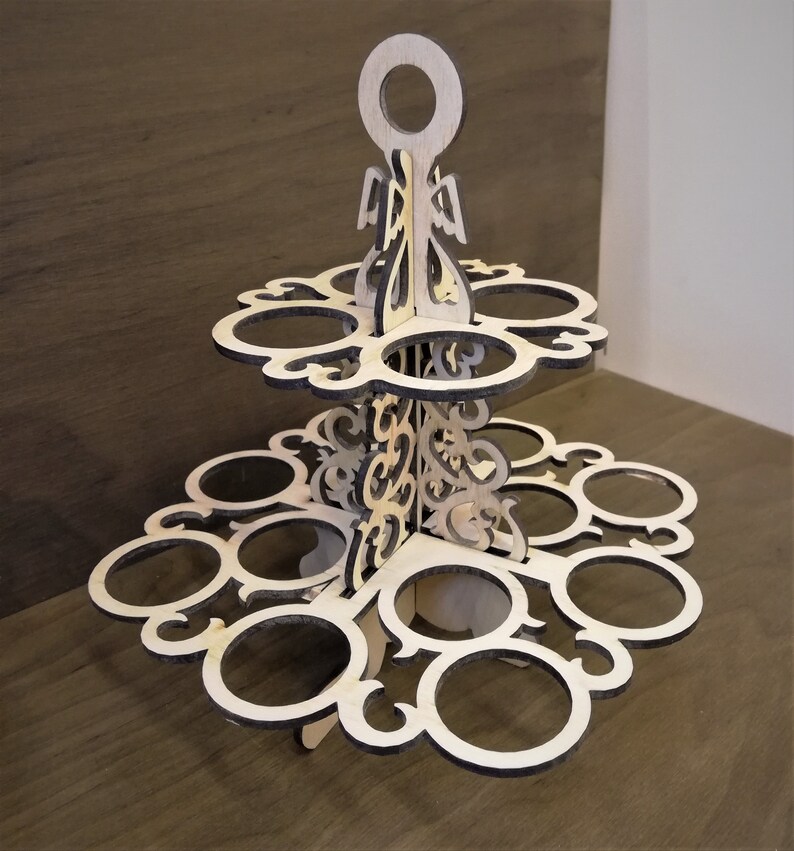 May include: A two-tiered wooden stand with a decorative design. The stand has a handle on top and 12 circular cutouts for holding items.