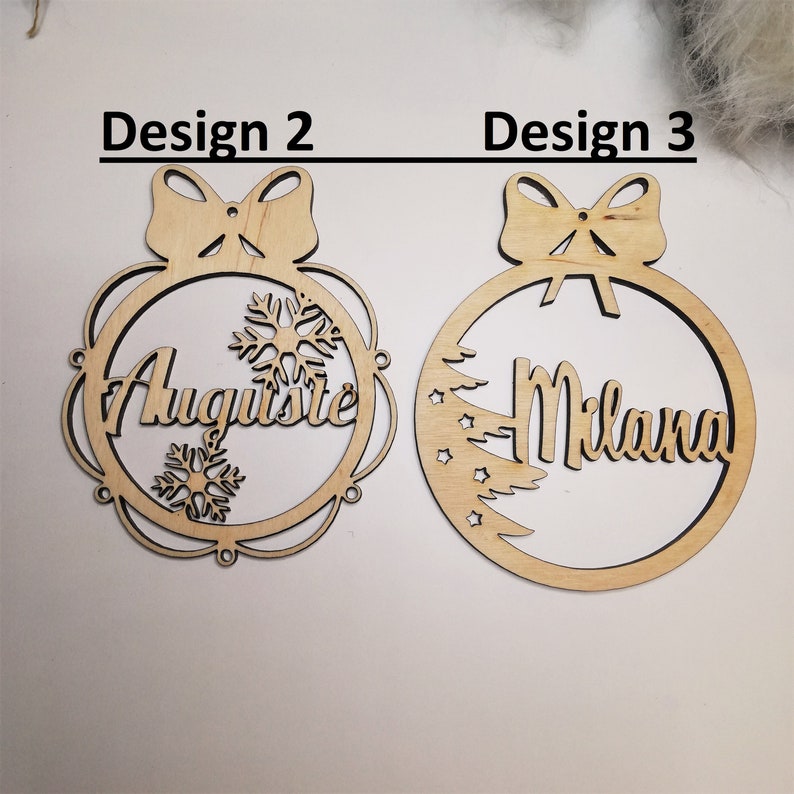 May include: Two wooden Christmas ornament designs. The first design features a snowflake and the name "Auguste". The second design features a stylized Christmas tree and the name "Milana".