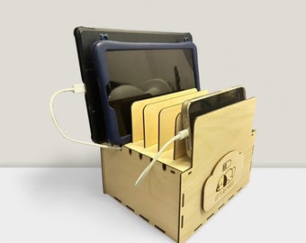 May include: A wooden charging station with slots for tablets and smartphones, with devices connected to charging cables. The station features a cloud-shaped logo and the text "LET'S RECHARGE".
