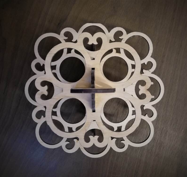 May include: A wooden cupcake stand with a decorative design. The stand has six circular cutouts for cupcakes and a central base.