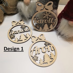May include: Three wooden Christmas ornaments with a snowflake and tree design. The ornaments are personalized with the names "Karolis", "Daniela", and "Aron".