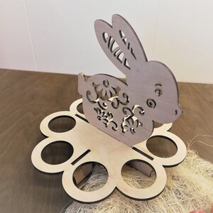 May include: Wooden Easter egg holder shaped like a bunny with floral details. The holder has six egg-shaped slots.