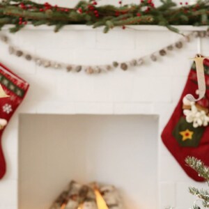 May include: Two red Christmas stockings with white trim and a snowman design hang from a white fireplace mantel. The stockings are decorated with gold stars and snowflakes. A garland of white beads hangs above the stockings.