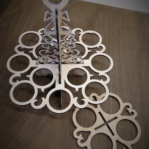 May include: Wooden stand with a decorative design, featuring multiple circular cutouts for holding items. The stand is made of light brown wood and has a unique, intricate pattern.
