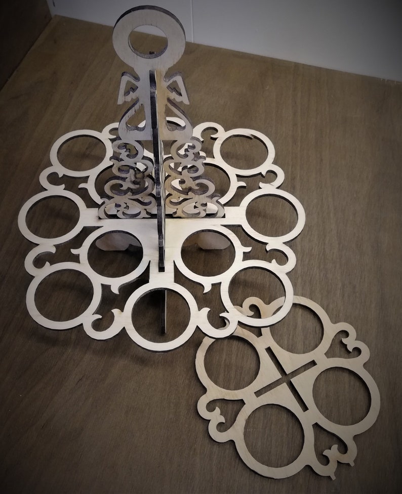 May include: Wooden stand with a decorative design, featuring multiple circular cutouts for holding items. The stand is made of light brown wood and has a unique, intricate pattern.