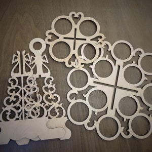 May include: Two wooden cutout designs for holding cups or glasses. The larger design has eight circular cutouts and the smaller design has six circular cutouts. Both designs have intricate patterns.